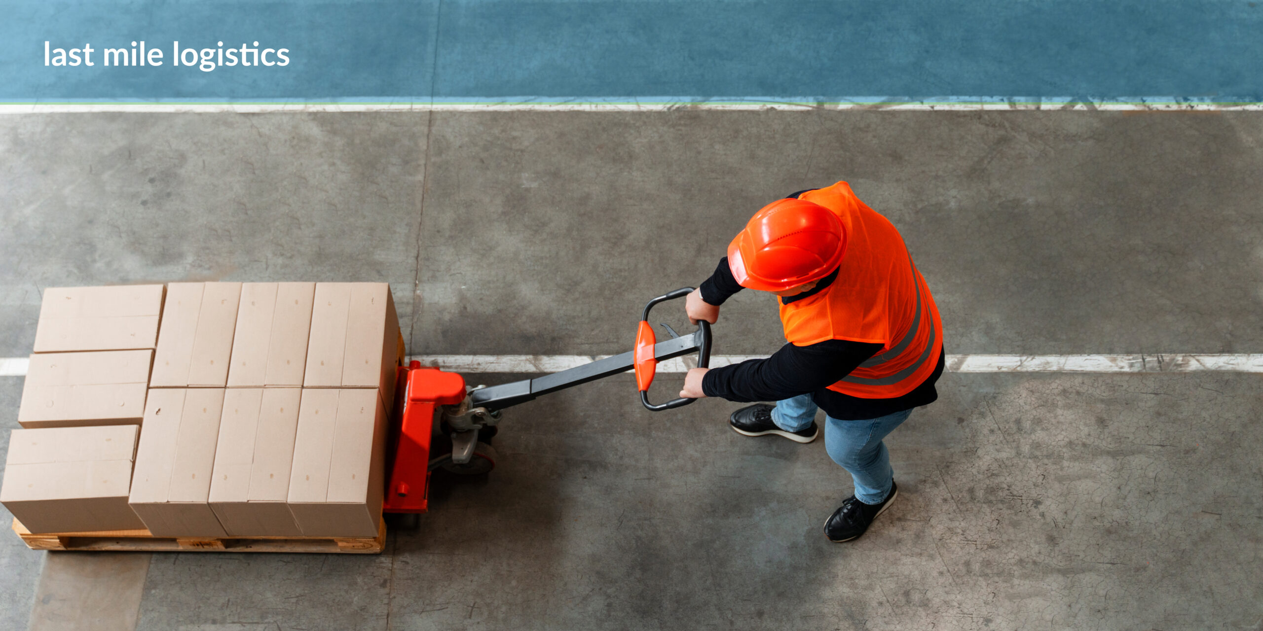 A worker in an orange safety vest and helmet using a manual pallet jack to move a stack of cardboard boxes on a wooden pallet, with the text 