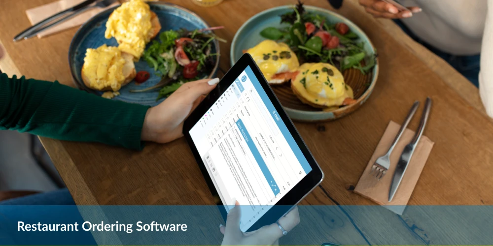 Person using a tablet with restaurant ordering software at a table with breakfast dishes.