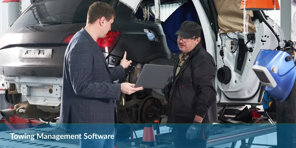 Two individuals with a laptop stand in a garage near a disassembled car, with text "Towing Management Software."