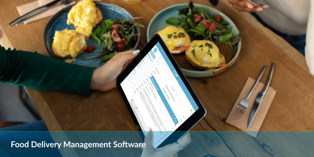 Person using tablet with food delivery management software beside breakfast dishes on a table.