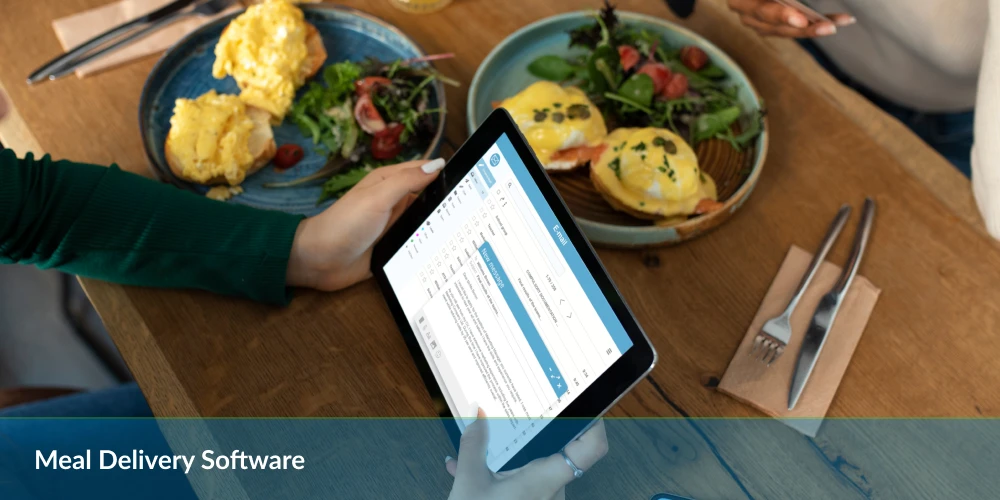 Person using a tablet with meal delivery software at a table with breakfast dishes.