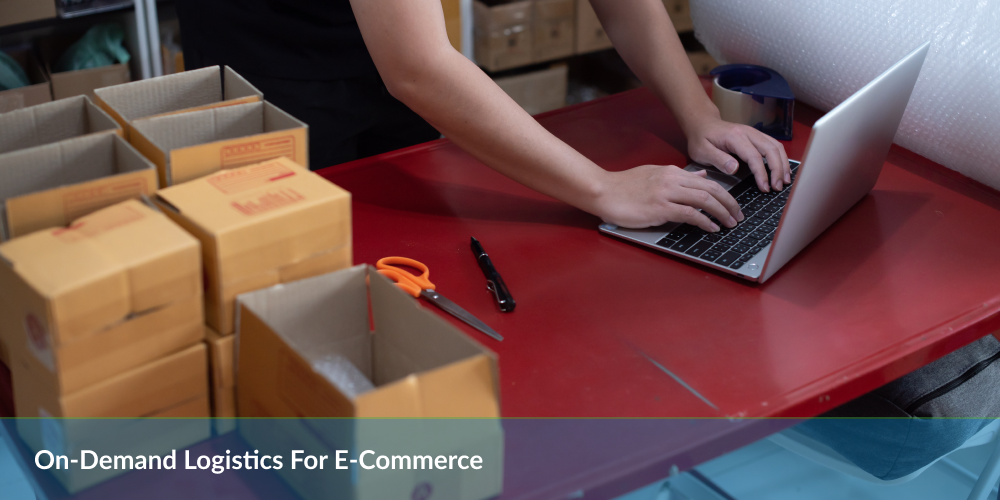 A person works on a laptop at a table cluttered with cardboard boxes and packing materials, illustrating e-commerce logistics.