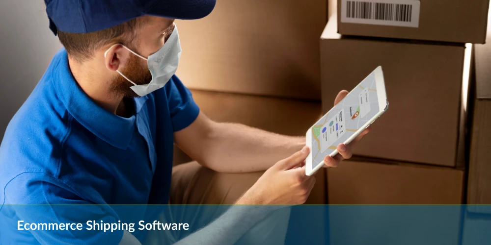 A worker in a blue shirt holds a tablet, checking shipping software, surrounded by stacks of shipping boxes in a warehouse setting.