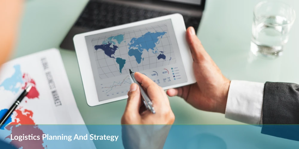A person analyzing logistics data on a tablet, displaying a world map and graphs, with strategy documents nearby.