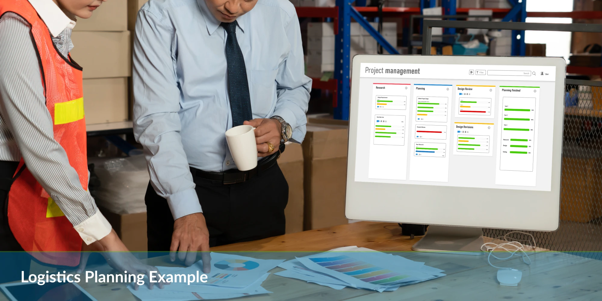 A man in a dress shirt and a woman in safety gear discuss logistics plans, while a computer displays a project management interface.