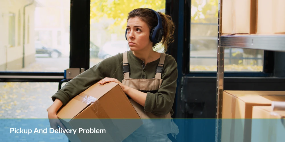 A woman in work overalls and headphones holds a box indoors, illustrating the pickup and delivery problem. Shelves and a glass door are visible behind her.